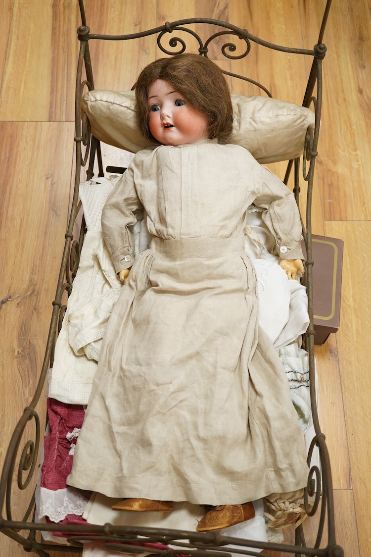 An Heubach Koppelsdorf bisque doll, mould 320 with sleeping eyes, open mouth and jointed composition body, together with a tubular and wrought metal half-tester bed, on casters, related clothing and bedding, doll 64cm